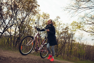 Young woman having fun near countryside park, riding bike, traveling at spring day. Calm nature, spring day, positive emotions. Sportive, active leisure activity. Walking in motion, blossoming nature.