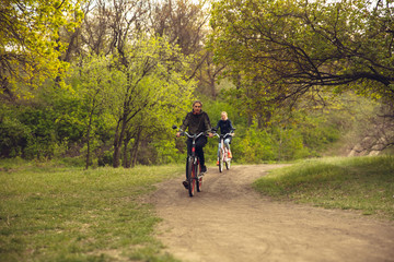 Fototapeta premium Best friends having fun near countryside park, riding bikes, spending time healthy. Calm nature, spring day, positive emotions. Sportive, active leisure activity. Traveling or walking together.