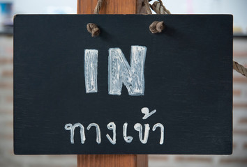 A pavement sign that says &lsquo;IN&rsquo; and Thai languages on cafe or restaurant hang on a wooden post at entrance.

