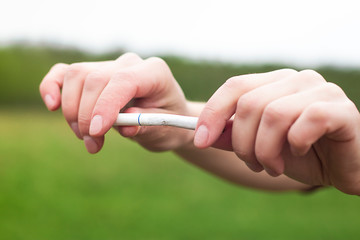 Broken cigarette in human hands, person man or woman is going to break apart a cigarette on green...