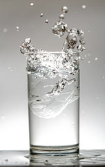 Close-up photo of the ice falls into the water glass causing water to splash out and the white background