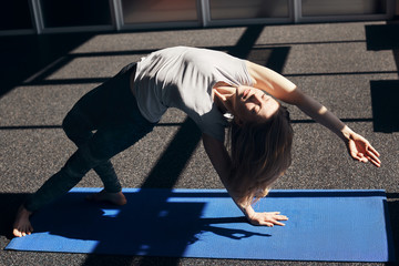 The girl does an asana with a bend back, leans on her legs and one hand, the second hand is raised...