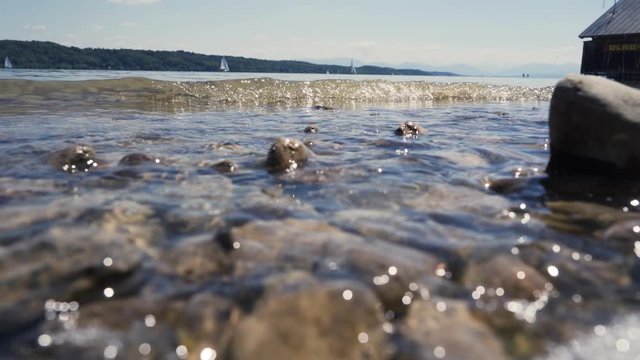 Closeup of the shore at Starnberger See. Lake near Munich and the Alps. Small waves playing with the shore stones, reflecting the summer sun.