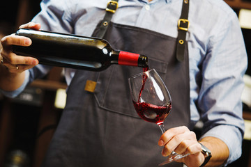 Male sommelier pouring red wine into long-stemmed wineglasses.