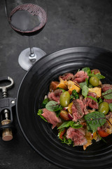 Salad with veal, olives, herbs on black background