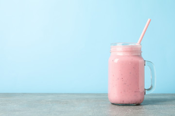 Glass jar of strawberry milkshake on gray table against blue background