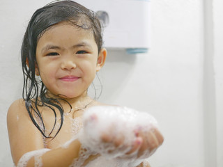 Little baby girl, 3 years old, enjoys making a lot of soap foam / bubbles in a bathroom at home -...