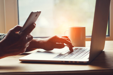 old senior successful woman working from home office, typing on laptop and using smartphone