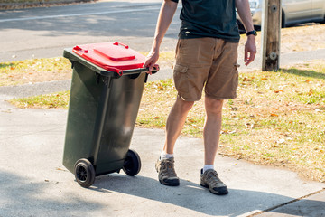 A man dragging the household wheelie red bin with general waste on the street for council gargbage...