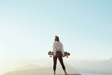 .Young long boarder woman with dreadlocks  standing on top of mountain in beautiful scenic nature in Montenegro at sunset. Freedom concept.