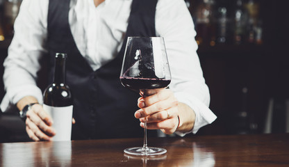 Sommelier holds out a glass of red wine at the bar, close-up.