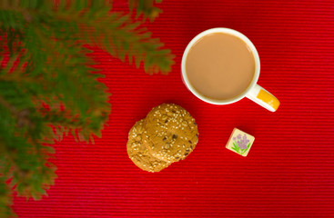 Good morning, this is coffee with milk, oatmeal cookies and candy in nature. Cup of coffee on a red photo with fir spruce branches