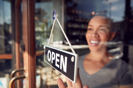 Female Owner Of Start Up Coffee Shop Or Restaurant Turning Round Open Sign On Door