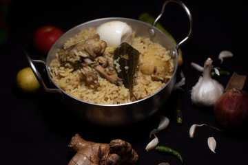 Indian spicy dish Biryani with egg, potato and Chicken in a pot along with ingredients in dark copy space background. Food and object photography.