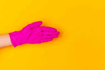 Hand in pink protective rubber glove greeting isolated on yellow studio background with copyspace. Gesturing, holding, presenting things. Negative space for your advertising. Showing, pointing.