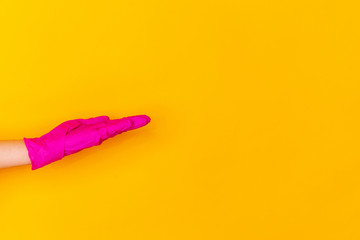 Hand in pink protective rubber glove taking, showing isolated on yellow studio background with copyspace. Gesturing, holding, presenting things. Negative space for your advertising. Showing, pointing.