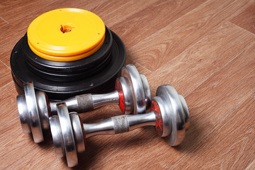 two dumbbells are lying on the floor next to the bar disks in the gym. Place for text.