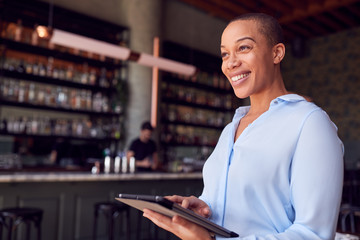 Confident Female Owner Of Restaurant Bar Standing By Counter Holding Digital Tablet
