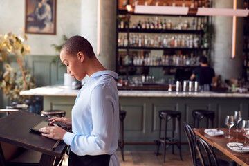 Female Owner Of Restaurant Bar Standing At Counter Using Digital Tablet