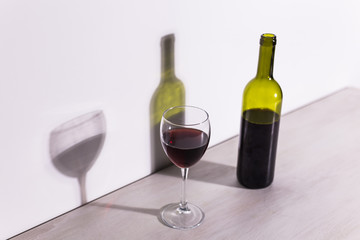 A glass of wine and a bottle casts a long shadow from the evening sun.