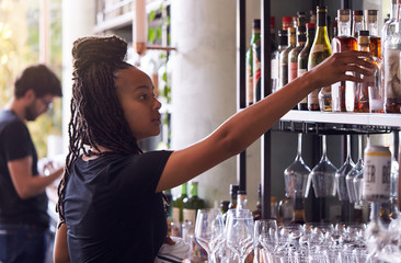 Female Bartender Arranging Bottles Of Alcohol Behind Bar