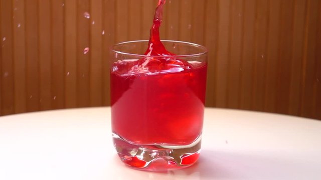 Pieces of ice fall in a glass with raspberry lemonade standing on a white table, slow motion