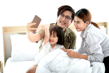 Happy family having fun and spending time together in the bedroom, father, mother and daughter using mobile phone take selfie, parents and kid taking photo to keep in good memory at home
