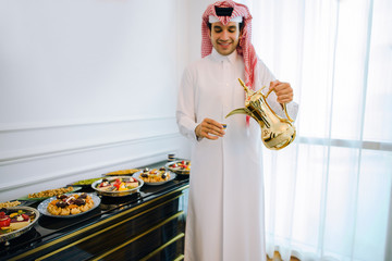 
Arab man in traditional white clothes pour tea on Iftar and eat Arab sweets