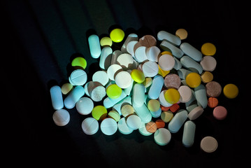 White, yellow, red, orange and blue pills on a black cardboard background. Medication on a dark background with contrasting dramatic light.