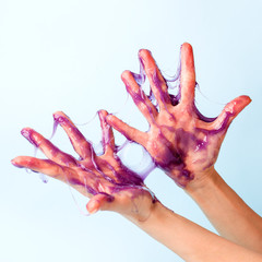 Young girl hands with sticky purple slime on blue background, liquid wax for depilation, conceptual...