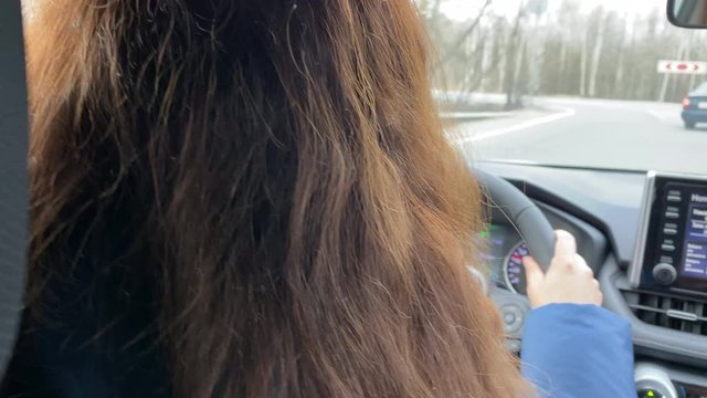 Rear view of brunette woman driving her car through the city streets, female driver behind the wheel of SUV