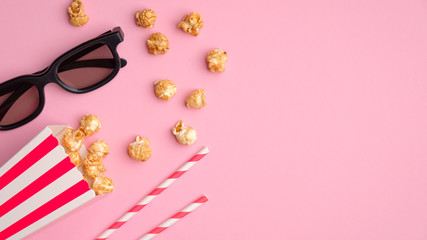 Pop corn in striped red and white cardboard box, 3d glasses, drink straws on pink table top view. Online cinema, watching movie concept.