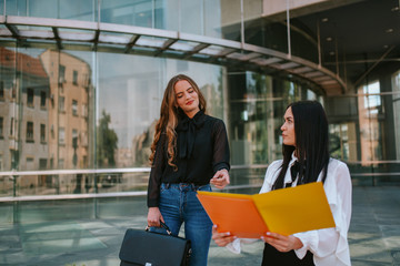 Two beautiful attractive caucasian business women stand in front of the company. Business and fashion