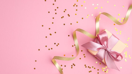 Fashion gift box with pink ribbon bow, golden streamer and confetti star on pink background top view. Flat lay composition for birthday, christmas or wedding.