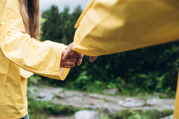 Hands of man and woman in yellow raincoats close-up.