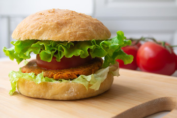 Vegan burger with chickpea bean patty, lettuce, vegan mayonnaise, tomatoes, pickles and homemade bun with sesame seeds on a wooden board
