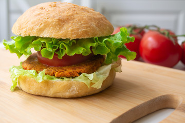 Vegan burger with chickpea bean patty, lettuce, vegan mayonnaise, tomatoes, pickles and homemade bun with sesame seeds on a wooden board