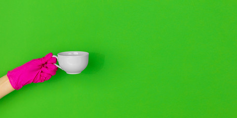 Hand in pink protective glove with coffee cup isolated on green studio background with copyspace. Gesturing, holding, presenting things. Negative space for your advertising. Showing, pointing.