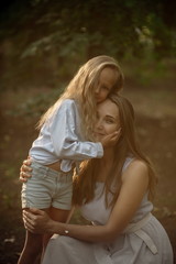 Beautiful girl 7 years old with long blonde hair with a blonde mom walk and cuddle at sunset in the summer park
