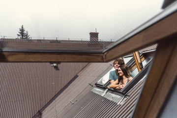 A man and a woman look out of the windows of a house in the mountains.