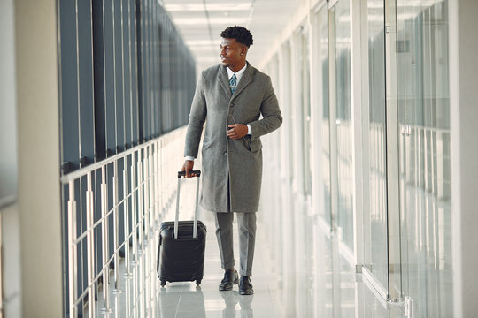 Black man at the airport. Guy with suitcase. Male in a black suit.