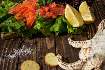 slices of red fish fillet on a wooden background. trout, lettuce, crackers, toasts, red pepper. preparing breakfast