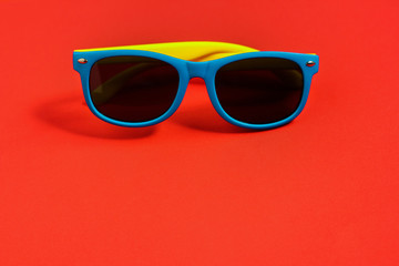 Children's sunglasses on red background. Summer holiday concept, minimalism