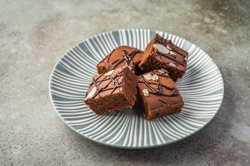 Homemade brownies with almond petals on a textured plate on a wooden background. Close up. Horizontal view