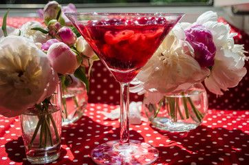 Magic solemn still life with glass of red drink with autumn organic berries surrounded by white flowers in the diagonal striped shadow of the blinds on a bright sunny day. Greeting card on textile