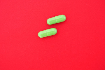 Two green capsules on an isolated red background. Concept of medical treatment.