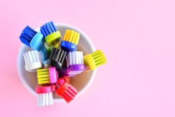 Colorful new plastic toothbrushes in white mug on pink neutral background, top view,  selective focus, copy space. Trendy health care concept 