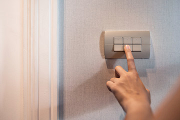 Asian woman finger is turning off on grey light switch over textile texture wall in the hotel. Copy...