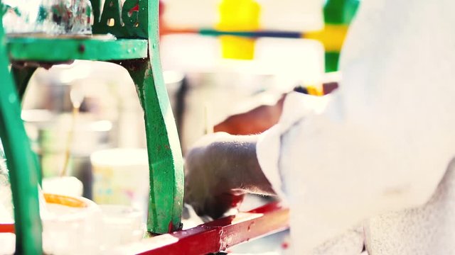 side view of indian ice gola maker spinning an ice gola between his hands having an ice grinding machine and bottles with colorful syrup in the background.