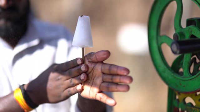 front view of indian ice gola maker spinning an ice gola between his hands having an ice grinding machine on the side.